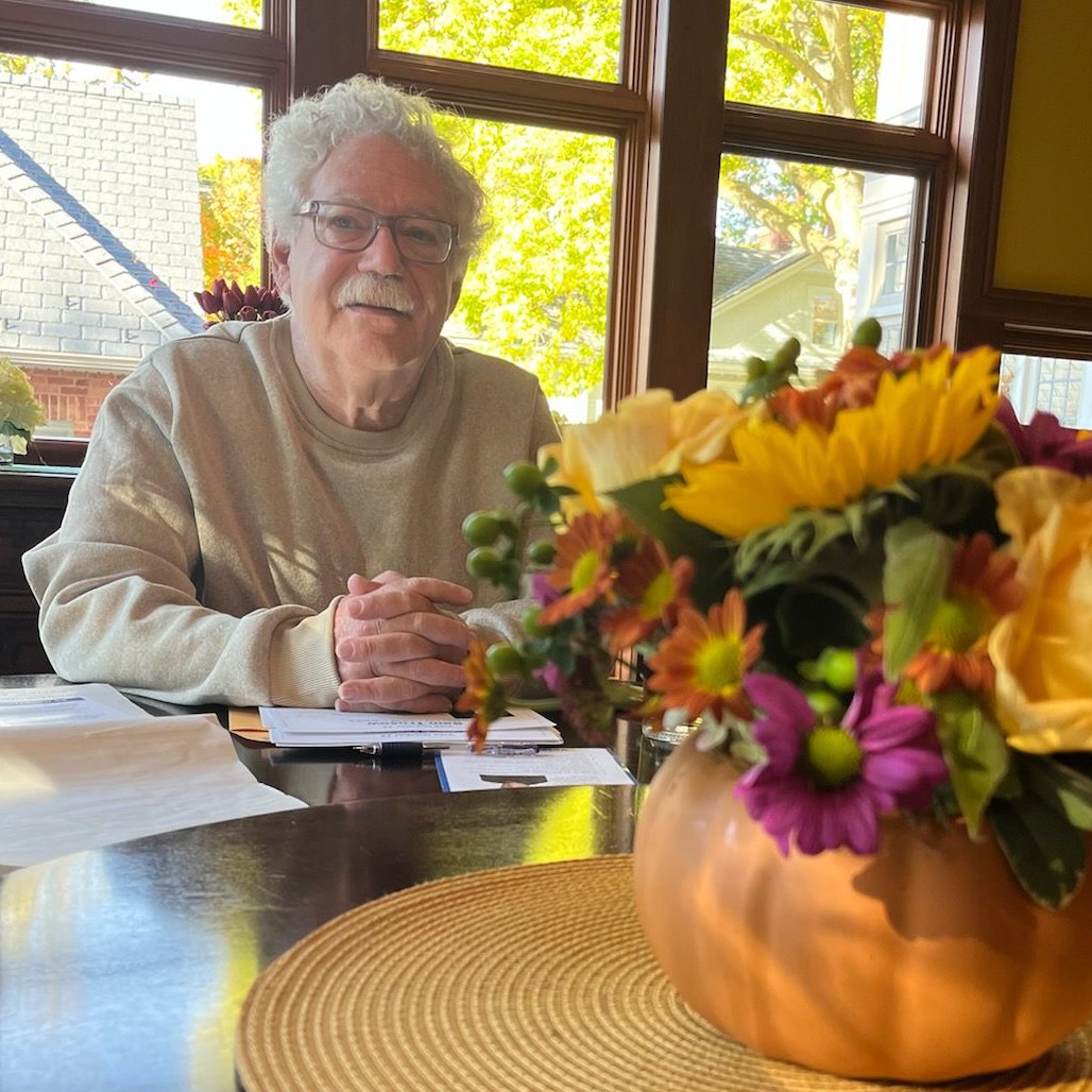 A picture of Sam, with a glass of flowers in the foreground.